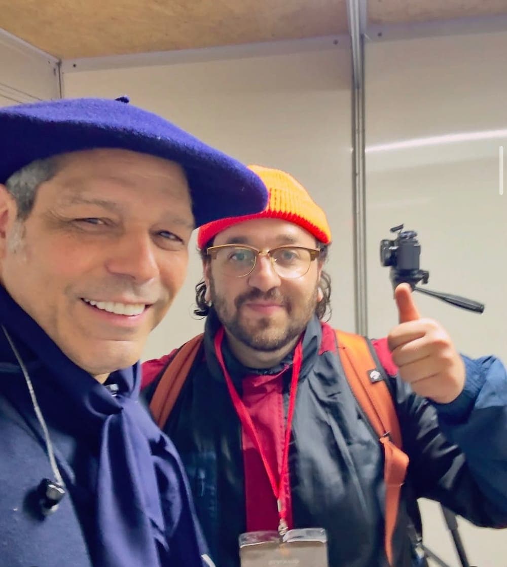 Mateus Rosa no bastidor, com a câmera no tripé e fazendo sinal de positivo